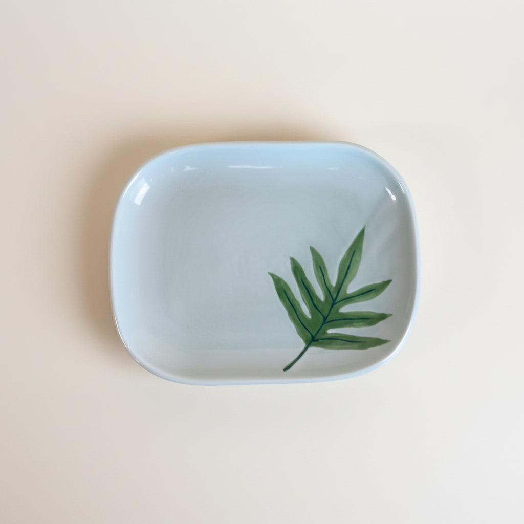 A ceramic plate with a lauae fern hand-painted design, presented on a wooden surface.