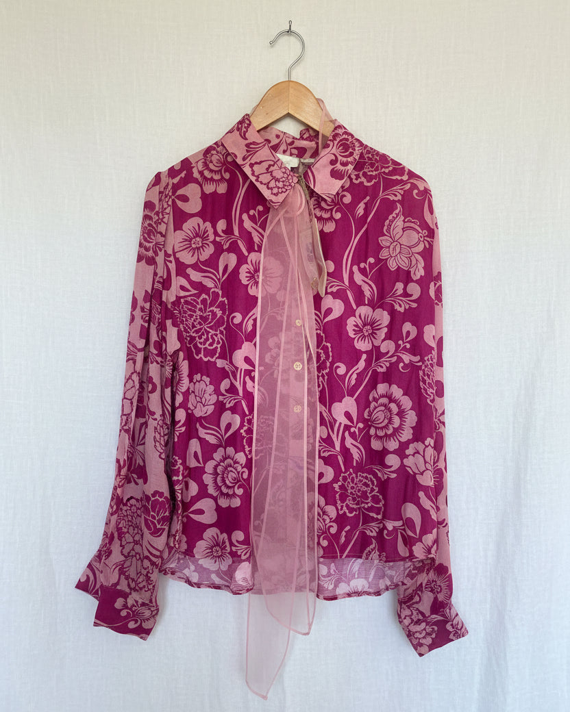 A pink shirt with a floral pattern and a matching scarf with a floral pattern, hanging on a wooden hanger.