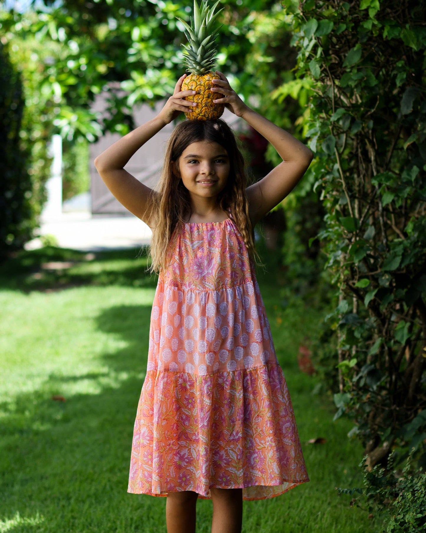 Young girl in a colorful dress holding a pineapple outdoors.