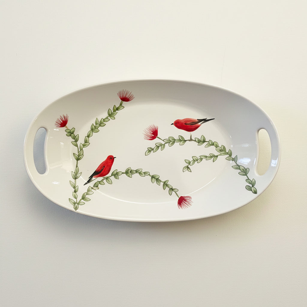 An oval white ceramic serving tray with side handles, decorated with painted red birds and green leafy branches on a light cream background.