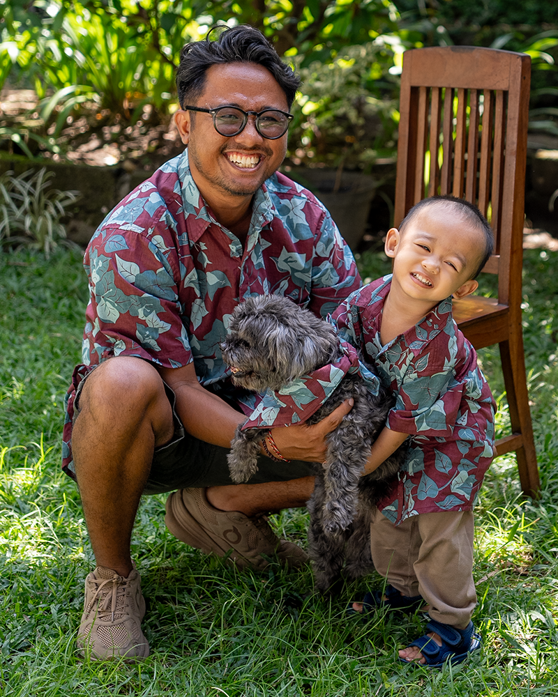 Man and child in matching aloha shirts with a dog outdoors on grass