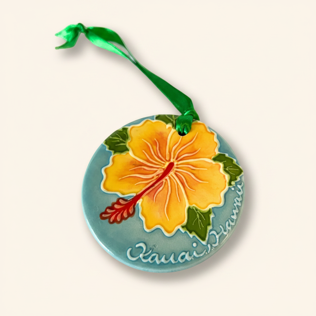 A hand-painted ceramic ornament shaped like a hibiscus flower with green leaves and pink petals, with the text 'Kauai Hawaii' and a signature below the flower.