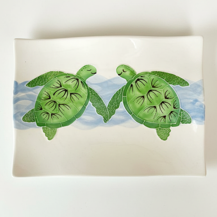 A square white ceramic serving platter featuring a painted illustration of two green sea turtles swimming in light blue water.