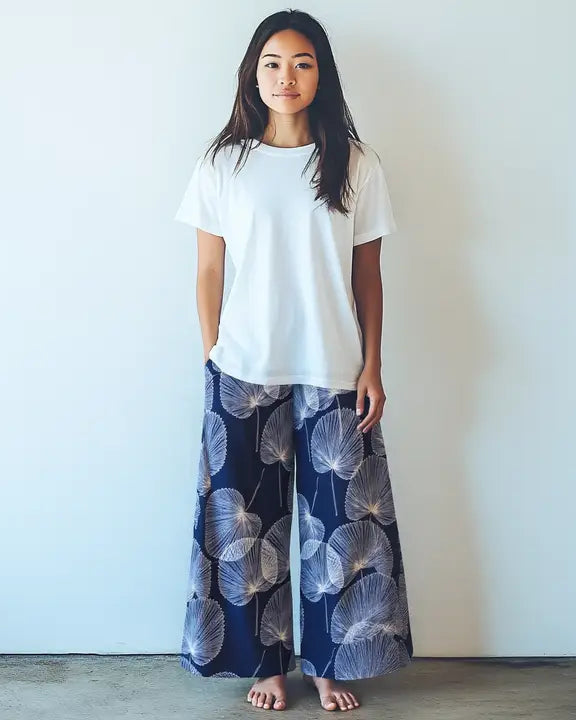 Woman wearing a white t-shirt and navy blue patterned pants against a plain background