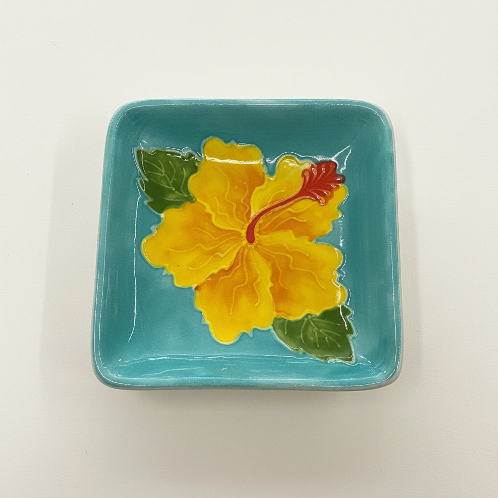 Square ceramic plate with a yellow flower design on a light blue background