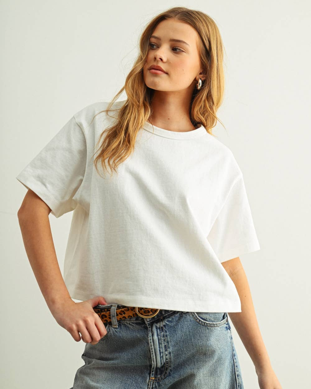 Woman wearing a white oversized t-shirt and blue jeans on a plain background