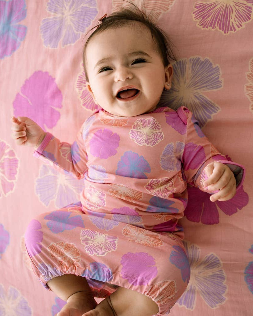 Baby in a pink floral outfit lying on a pink floral blanket