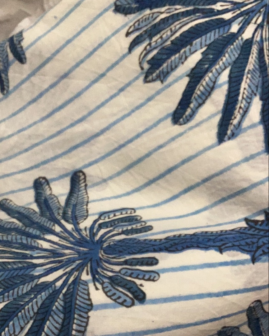 Close-up of a pareo sarong with a palm tree pattern in blue on a white striped background.