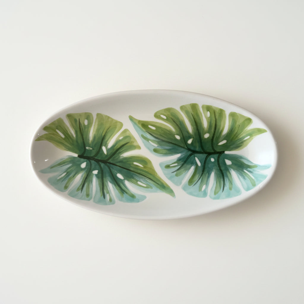 Oval ceramic plate with green leaf patterns on a gray background