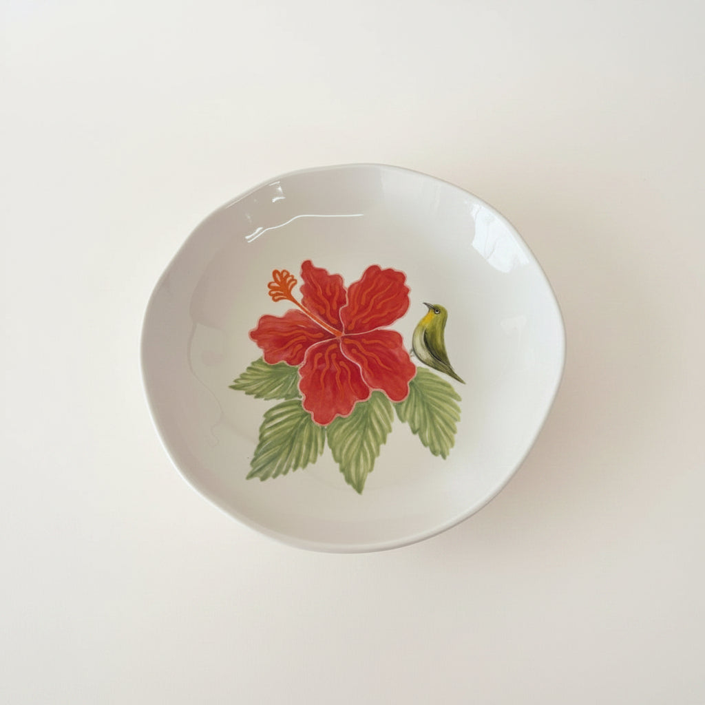 Round ceramic plate with a red flower and green leaves design on a white background
