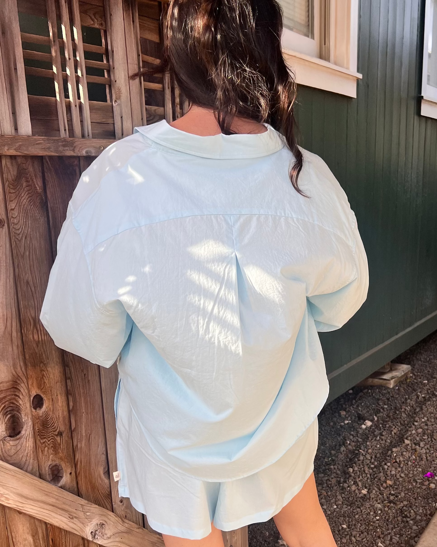 Woman wearing a light blue outfit standing outside a building with a wooden fence.