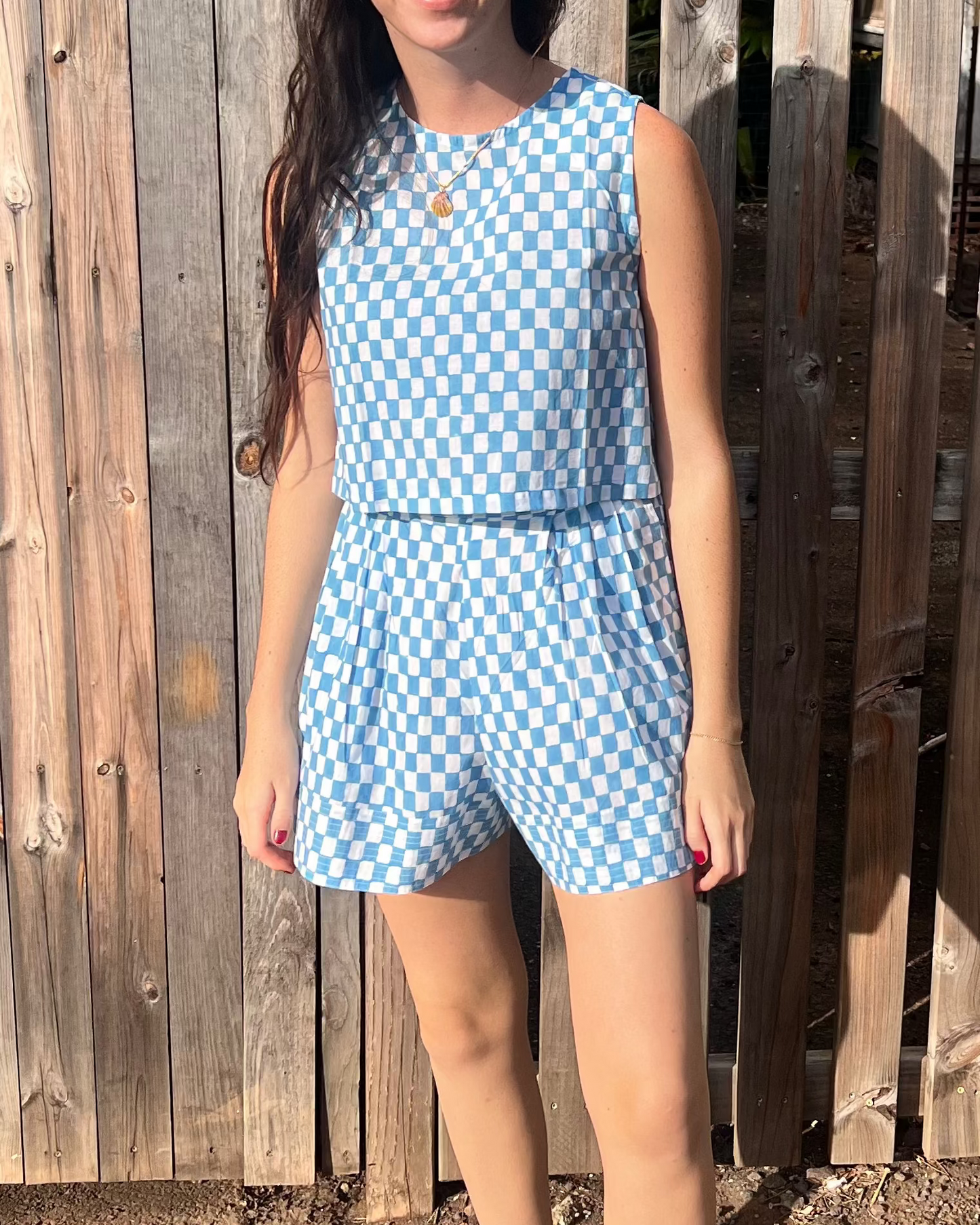 Woman wearing a blue checkered outfit standing in front of a wooden fence.
