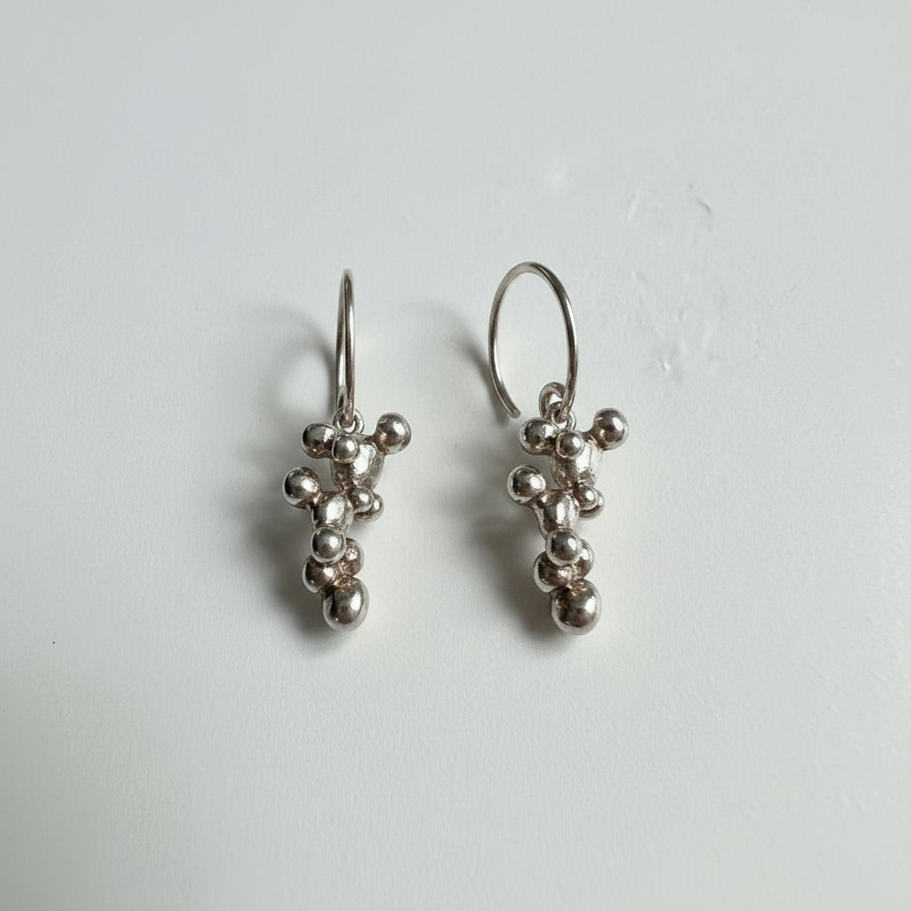 Silver earrings with bead-like charms on a plain background