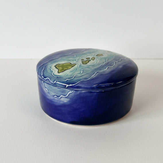Round blue ceramic box with a green design on a textured surface