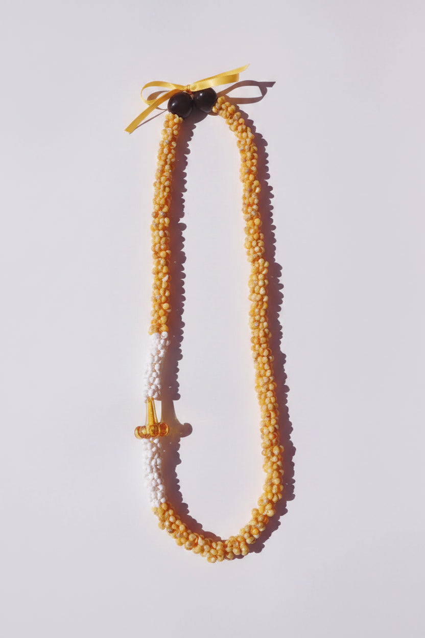 Beaded necklace with yellow bow and a puakenikeni on a white background
