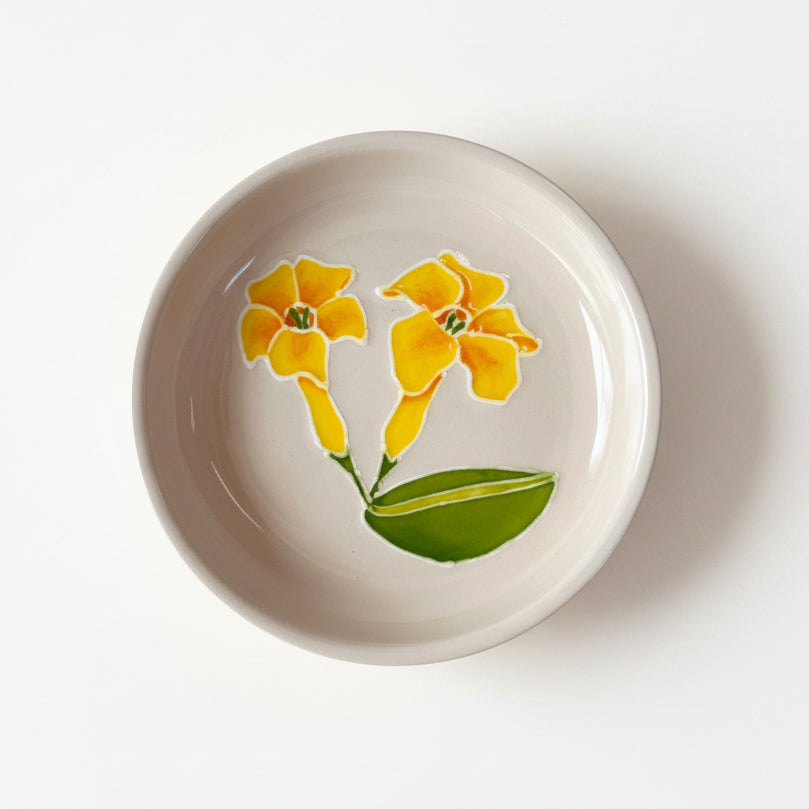 A hand-painted ceramic trinket dish with a floral design in yellow and green on a beige background.