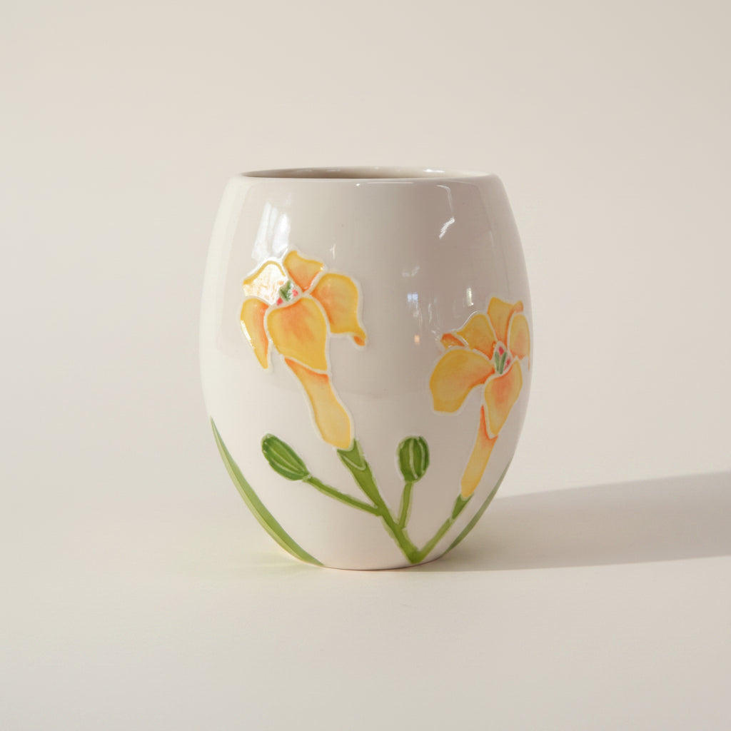 A beige ceramic cup with a yellow hibiscus design, hand-painted floral patterns, and green leaves.