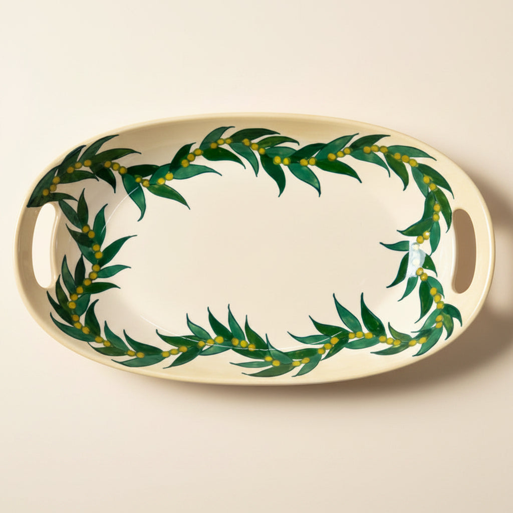 An oval ceramic serving platter with side handles, featuring a green leafy garland pattern with small yellow accents around the rim on a white background.