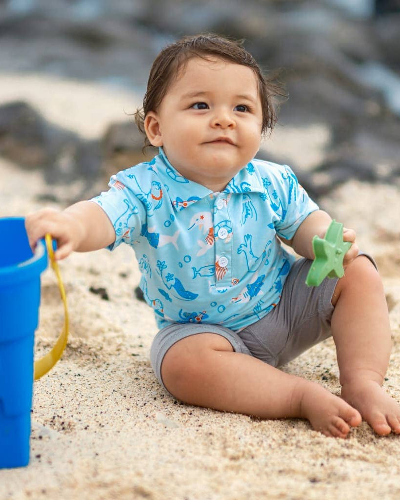 Child playing in the sand with a blue bucket and green starfish toy on a beach.