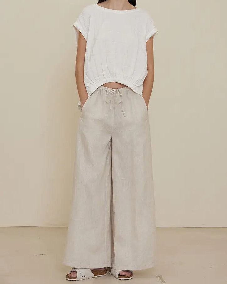 A model wearing long line linen pants with a wide fit and a white cropped top.