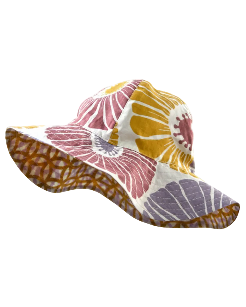 A multicolored patchwork sun hat with a floral design, featuring a Velcro chin strap and a lined rim, displayed on a stand.
