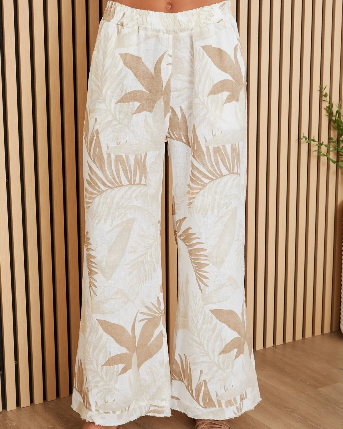 White pants with leaf pattern worn by a person against a wooden panel background
