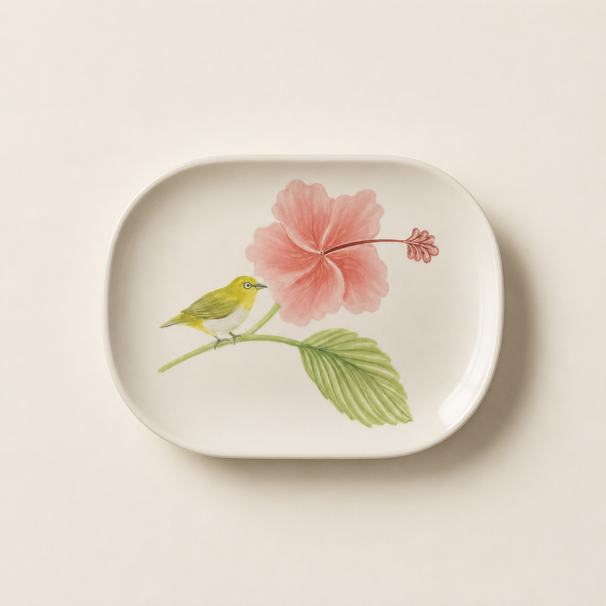 A white oval ceramic dish featuring a hand-painted botanical illustration of a pink hibiscus flower, green leaves, and a small yellow-green bird perched on a branch, set against a warm off-white background.