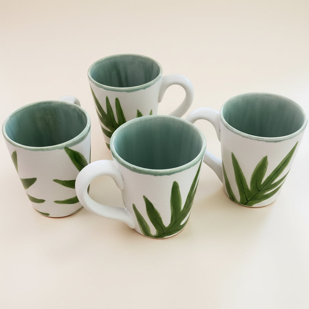 Four white ceramic mugs with green leaf patterns and pale green interiors, arranged on a light beige background.