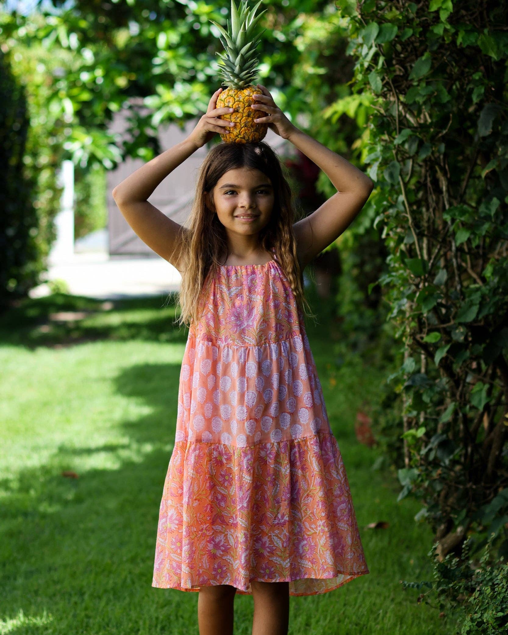 Young girl in a colorful dress holding a pineapple outdoors.