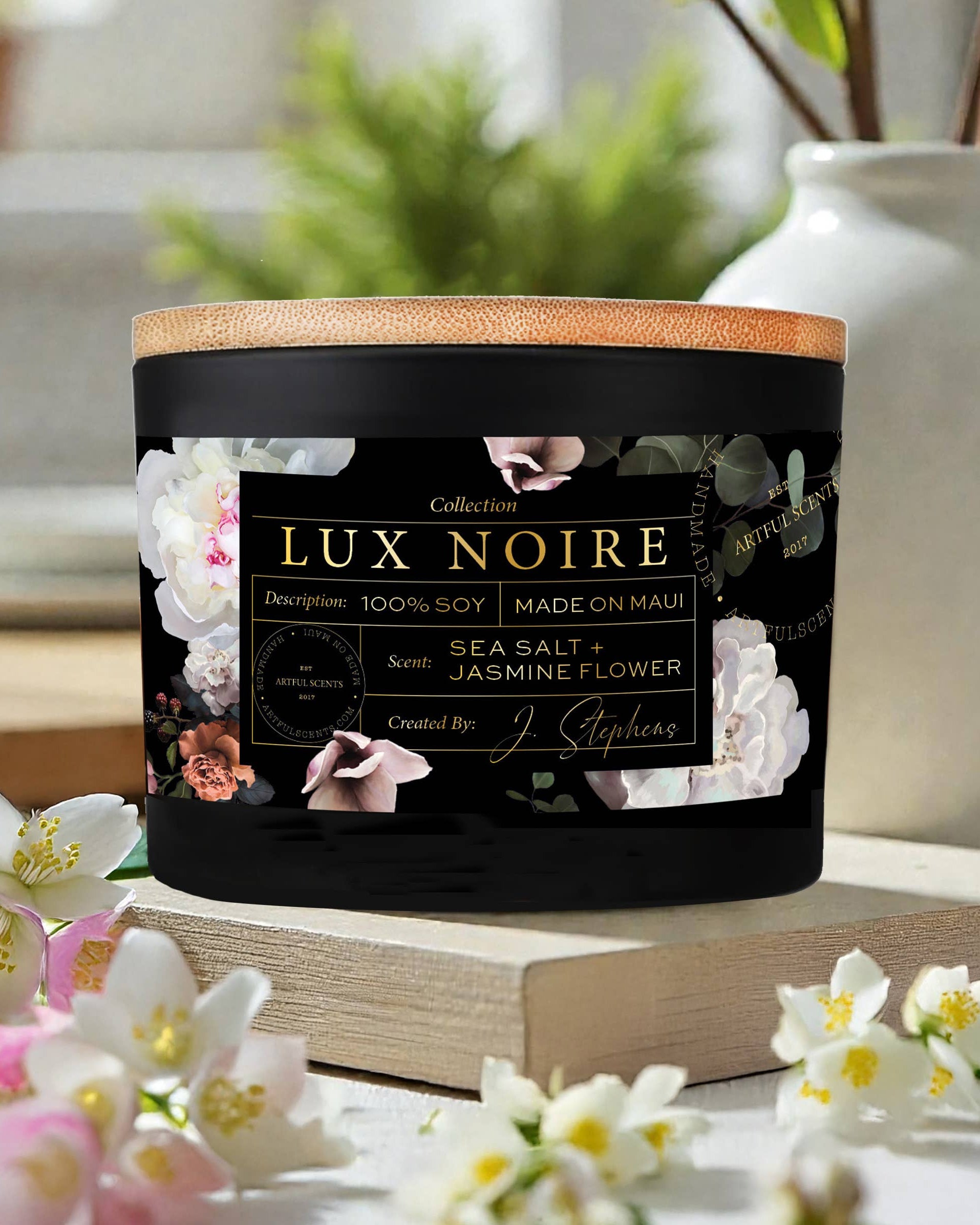 Lux Noire candle with floral design on label, surrounded by flowers and books.