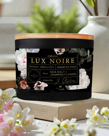 Lux Noire candle with floral design on label, surrounded by flowers and books.