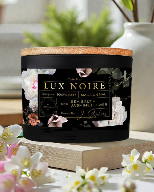 Lux Noire candle with floral design on label, surrounded by flowers and books.