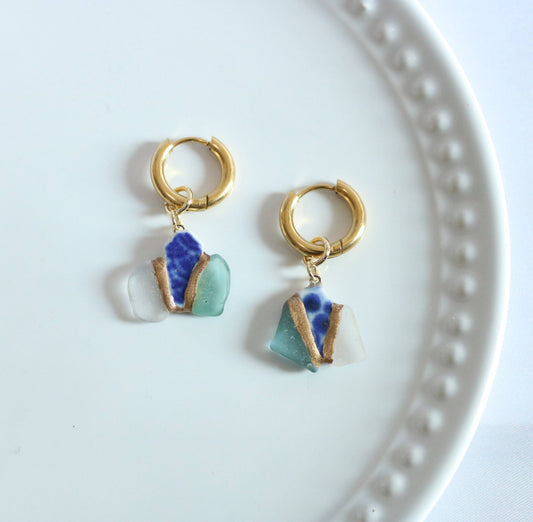 Gold hoop earrings with blue and green glass charms on a white plate.
