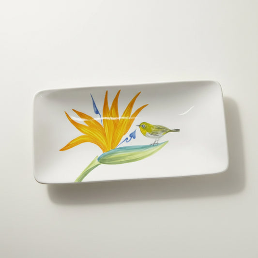 A white rectangular ceramic plate with rounded corners, featuring a painted illustration of a yellow-orange bird of paradise flower and a small green bird, shown on a light background with a soft shadow.