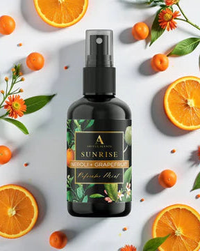 Bottle of 'Sunrise' body spray surrounded by oranges and leaves on a light background
