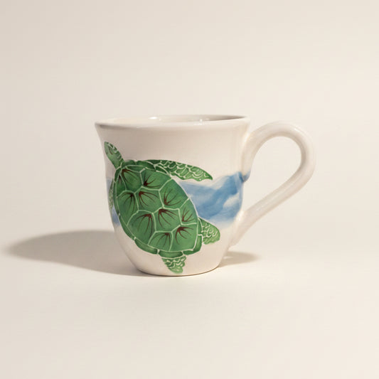 Ceramic mug with a green turtle design on a white shelf.