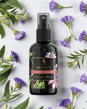 Black spray bottle with a label on a white background surrounded by green leaves and purple flowers