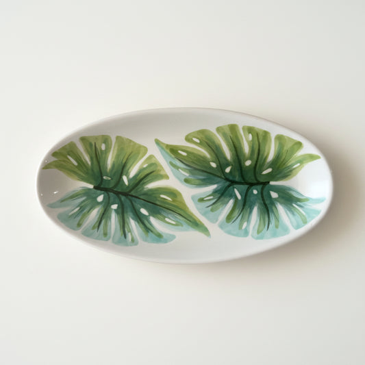 Oval ceramic plate with green leaf patterns on a gray background
