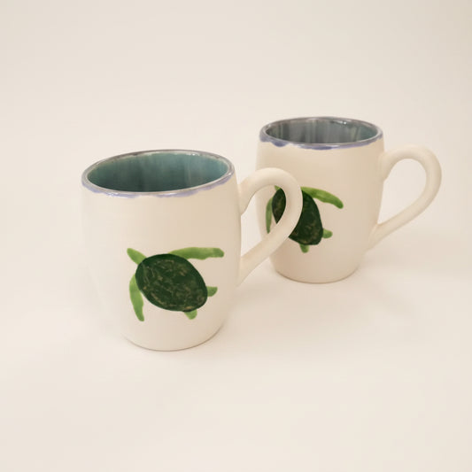 Two ceramic mugs with a turtle design and a celadon pattern on a table.