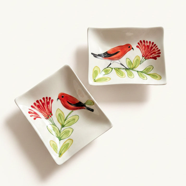 Two square white ceramic dishes with rounded corners, decorated with hand-painted red birds, red flowers, and green leaves, displayed on a light beige background.