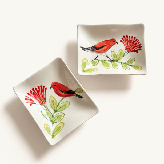 Two square white ceramic dishes with rounded corners, decorated with hand-painted red birds, red flowers, and green leaves, displayed on a light beige background.
