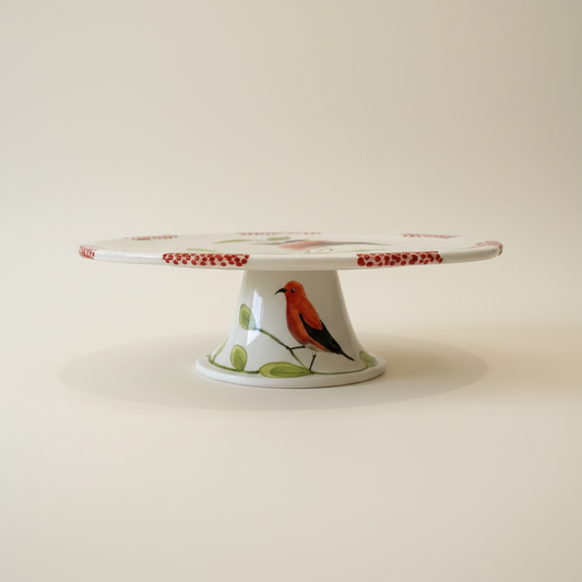 A white ceramic pedestal stand with a red bird and green leaves printed on the front, holding a long white rod with red dotted ends, set against a plain light gray background.
