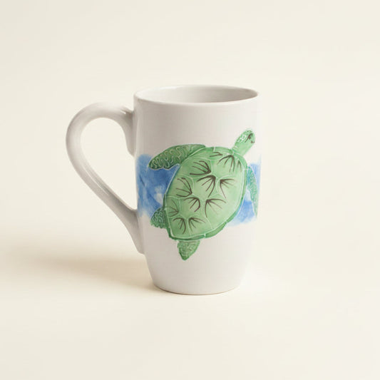 A white ceramic mug featuring a painted green sea turtle swimming in blue water, set against a solid off-white background.