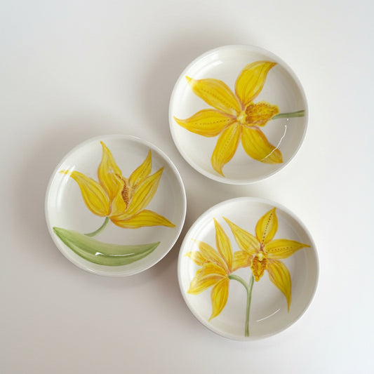 Three ceramic bowls with yellow floral designs on a gray surface
