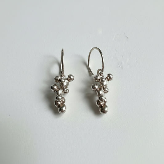 Silver earrings with bead-like charms on a plain background