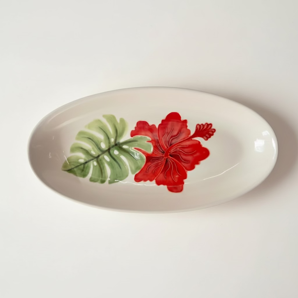 An oval ceramic plate with a hand-painted green Monstera leaf and a red Hibiscus flower.