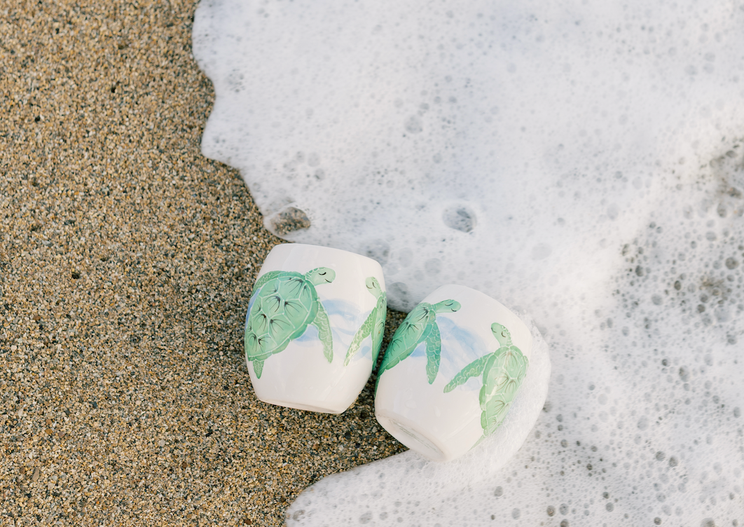 Two painted rocks on a beach with waves crashing around them.