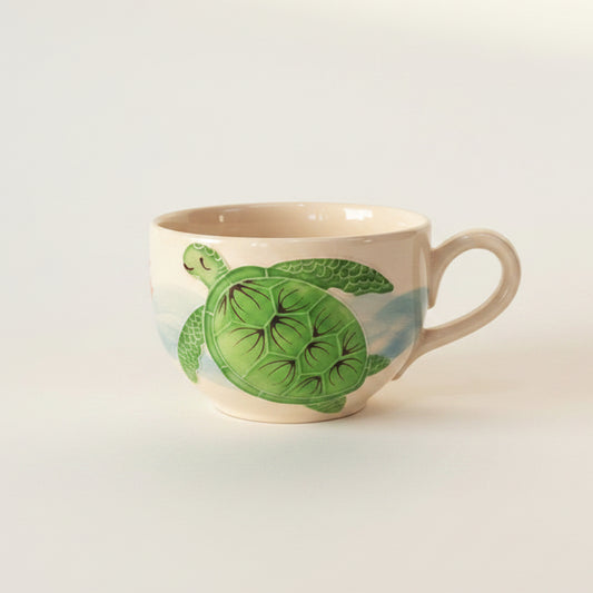 Two ceramic cups with a green sea turtle design on a light beige background, set against a plain white studio backdrop.