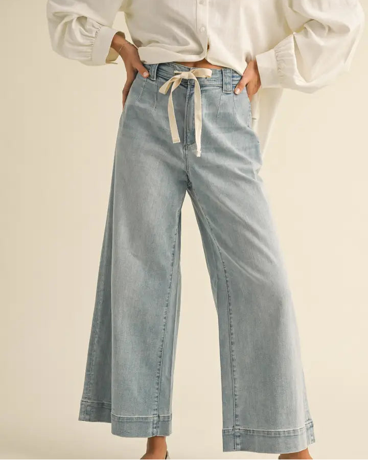 Person wearing a white blouse and light blue jeans with a beige background