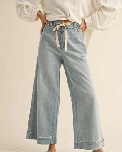 Person wearing a white blouse and light blue jeans with a beige background